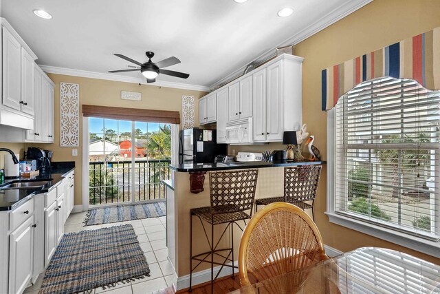 kitchen with light tile patterned floors, white cabinetry, black fridge, and ornamental molding