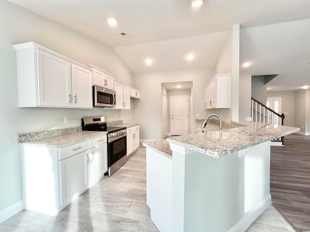 kitchen featuring lofted ceiling, kitchen peninsula, stainless steel appliances, white cabinets, and light stone counters