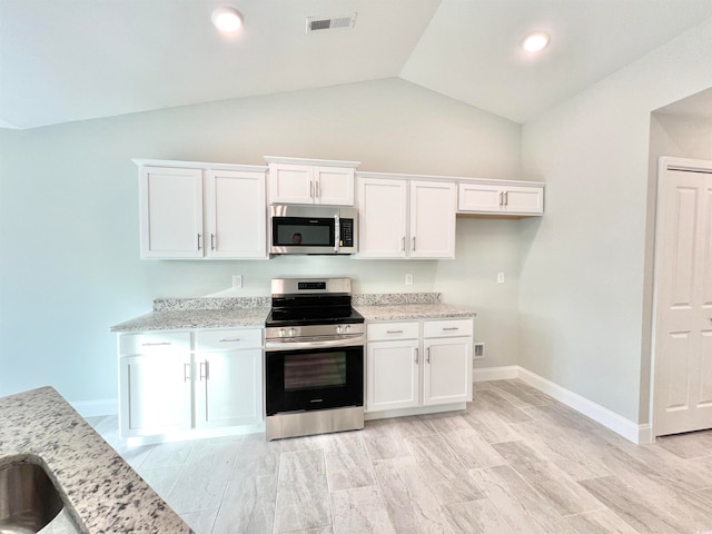 kitchen with vaulted ceiling, white cabinetry, light stone counters, and stainless steel appliances