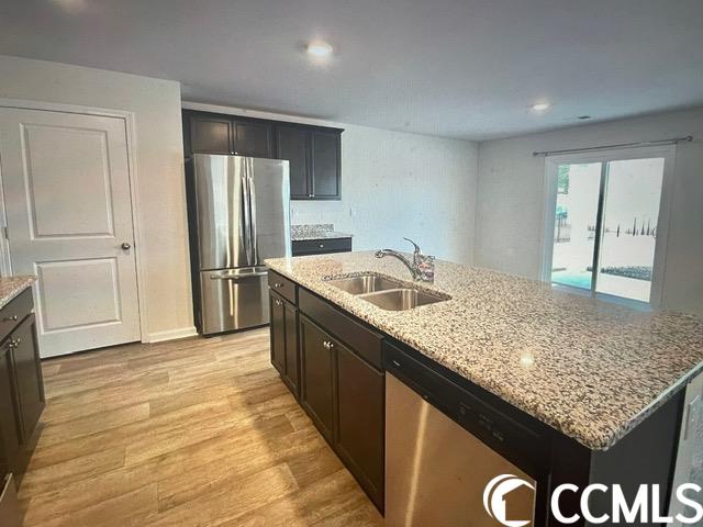 kitchen featuring light hardwood / wood-style floors, stainless steel appliances, sink, a kitchen island with sink, and light stone counters