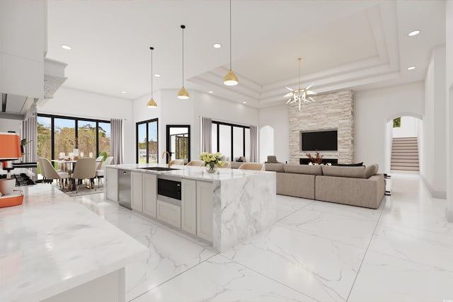 kitchen featuring light stone counters, a tray ceiling, a kitchen island with sink, and hanging light fixtures