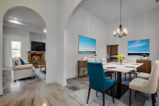 dining room featuring a stone fireplace, a chandelier, wood-type flooring, and a high ceiling