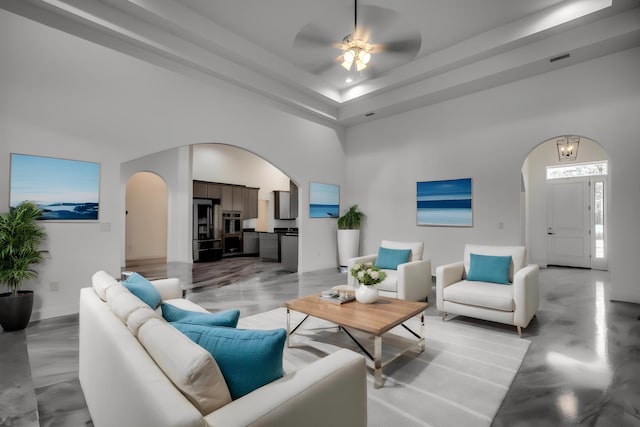 living room with a towering ceiling, ceiling fan, and a raised ceiling