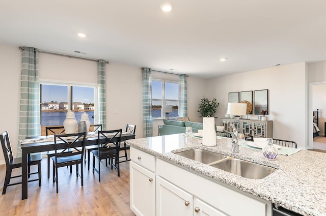 kitchen featuring white cabinets, light hardwood / wood-style floors, a water view, and light stone countertops