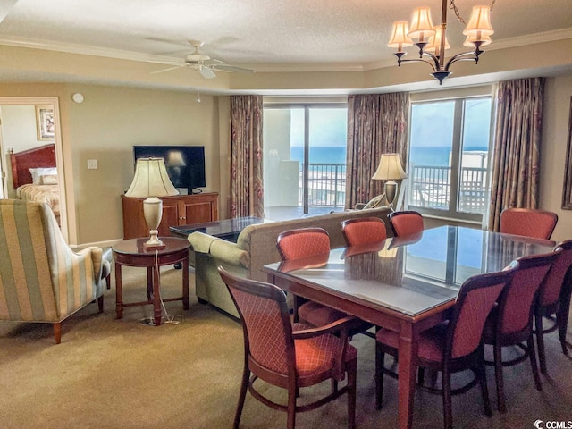 carpeted dining area with a water view, a wealth of natural light, ceiling fan with notable chandelier, and ornamental molding