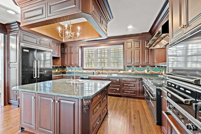 kitchen featuring light stone countertops, sink, an inviting chandelier, a center island with sink, and high end appliances