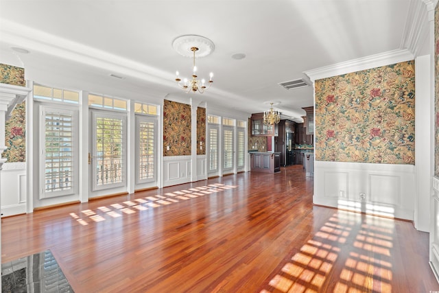 unfurnished living room featuring a notable chandelier, plenty of natural light, dark hardwood / wood-style floors, and ornamental molding