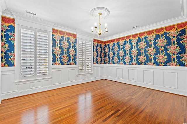 empty room with a healthy amount of sunlight, wood-type flooring, ornamental molding, and an inviting chandelier