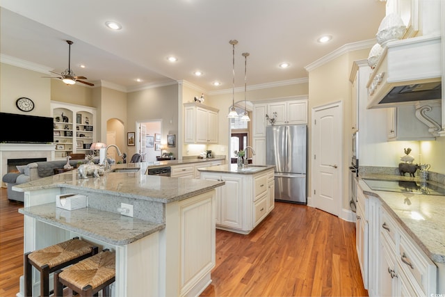 kitchen featuring decorative light fixtures, wood-type flooring, stainless steel appliances, and a large island with sink