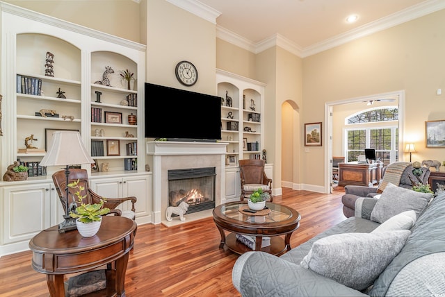 living room featuring built in shelves, light wood-type flooring, crown molding, and a high ceiling