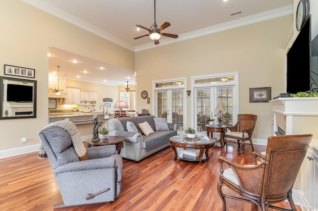 living room featuring french doors, crown molding, ceiling fan, a towering ceiling, and light hardwood / wood-style floors