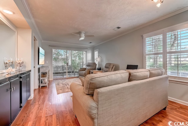 living room with ceiling fan, crown molding, light hardwood / wood-style flooring, and a textured ceiling