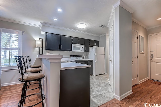 kitchen with white appliances, ornamental molding, a kitchen bar, and light tile floors