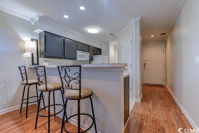 kitchen with a kitchen bar, ornamental molding, light hardwood / wood-style floors, and kitchen peninsula