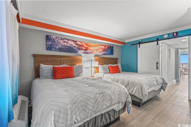 bedroom featuring crown molding, a barn door, and light hardwood / wood-style floors