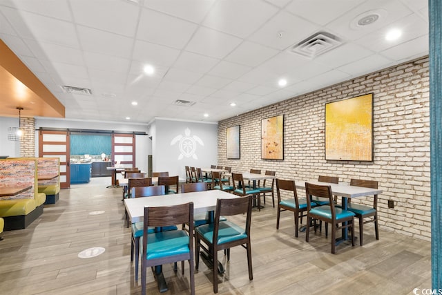 dining space featuring a barn door, brick wall, a paneled ceiling, and light wood-type flooring