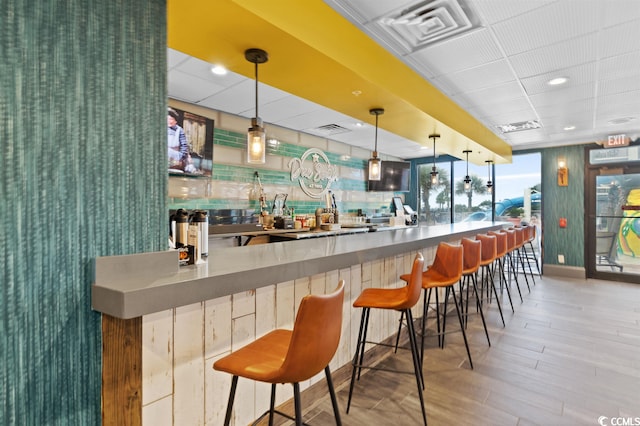 bar featuring light hardwood / wood-style flooring, pendant lighting, and stainless steel counters