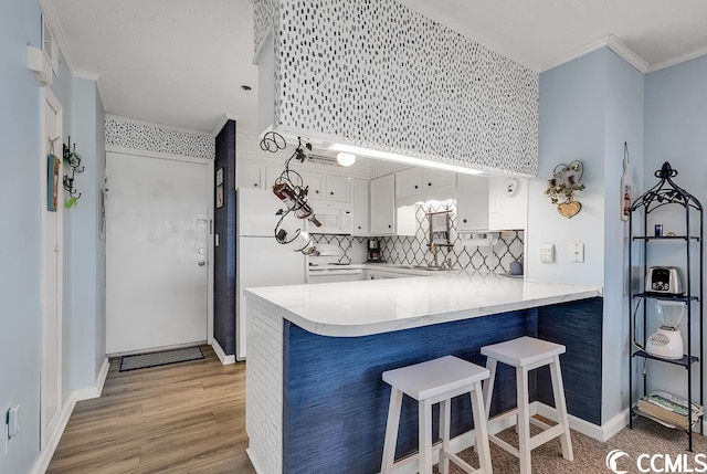 kitchen with light hardwood / wood-style floors, kitchen peninsula, tasteful backsplash, white appliances, and white cabinetry