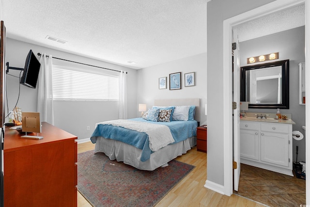 bedroom featuring connected bathroom, a textured ceiling, sink, and light wood-type flooring