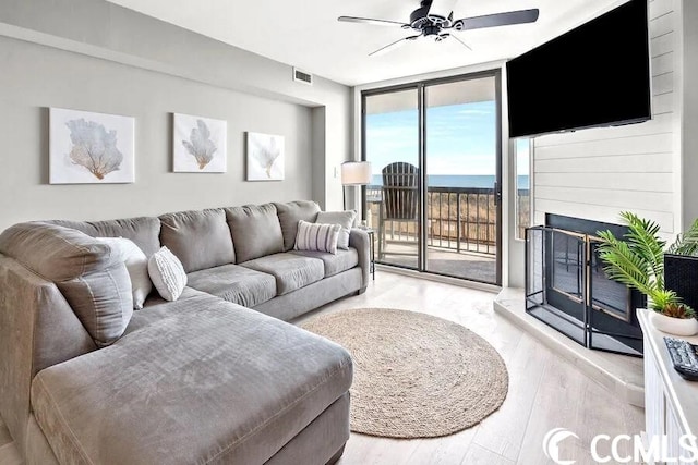 living room featuring ceiling fan, floor to ceiling windows, a water view, and light hardwood / wood-style floors