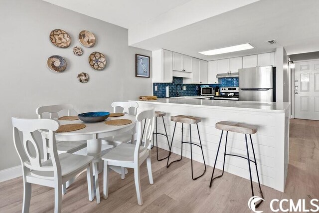 kitchen featuring light hardwood / wood-style floors, a breakfast bar, tasteful backsplash, appliances with stainless steel finishes, and white cabinets