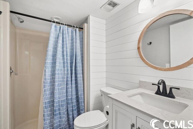 bathroom featuring vanity, wood walls, and toilet