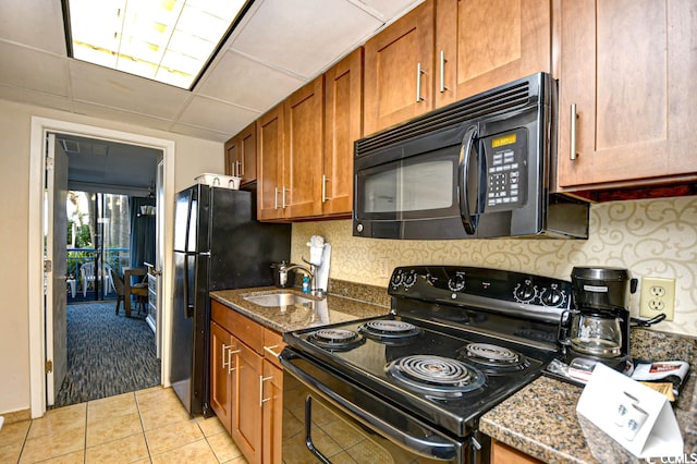 kitchen featuring dark stone counters, a drop ceiling, light tile floors, black appliances, and sink