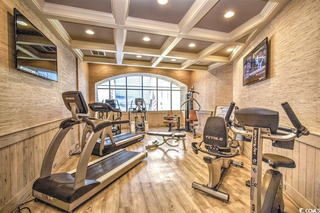 workout area featuring light hardwood / wood-style flooring, wooden walls, ornamental molding, and coffered ceiling