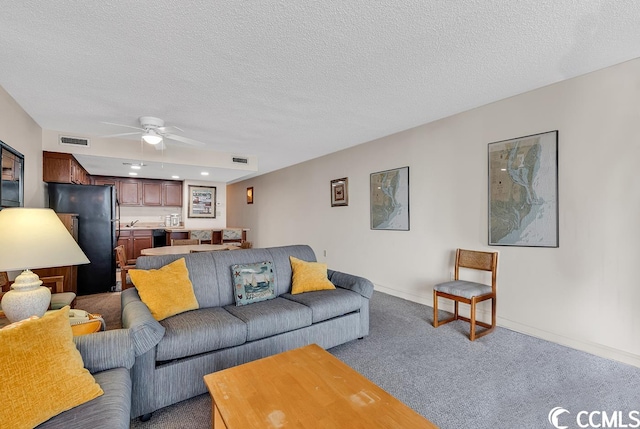 carpeted living room with ceiling fan and a textured ceiling