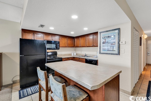 kitchen featuring light tile floors, a kitchen bar, a kitchen island, and black appliances