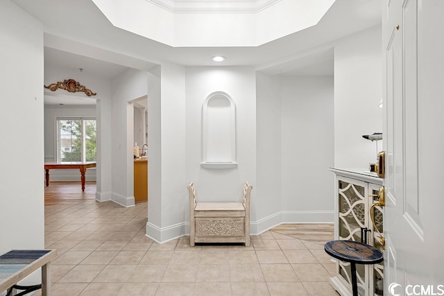 hall with a tray ceiling, crown molding, and light tile floors