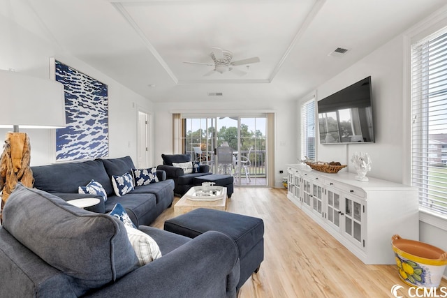 living room with light hardwood / wood-style flooring, a raised ceiling, and ceiling fan