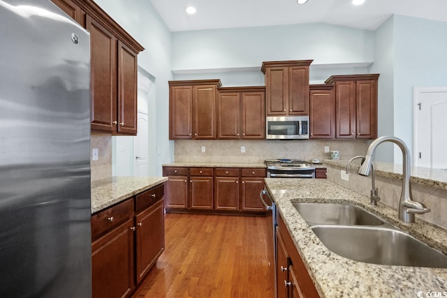 kitchen with light stone counters, stainless steel appliances, light wood-type flooring, lofted ceiling, and sink