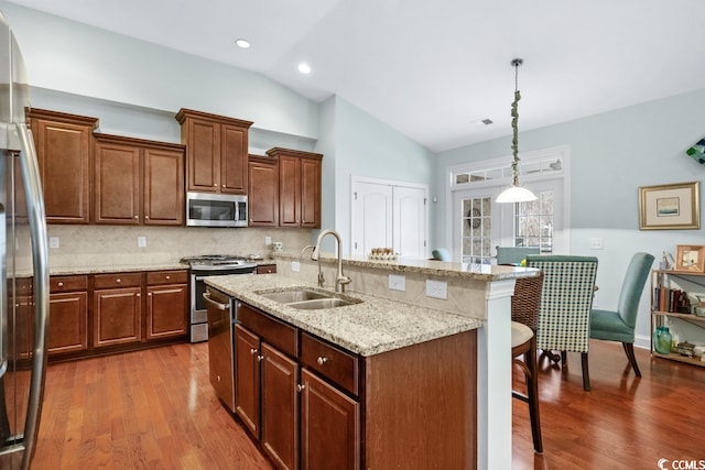 kitchen featuring decorative light fixtures, dark wood-type flooring, a breakfast bar, stainless steel appliances, and sink