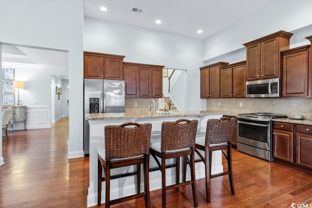 kitchen featuring a kitchen breakfast bar, appliances with stainless steel finishes, dark hardwood / wood-style floors, and light stone countertops