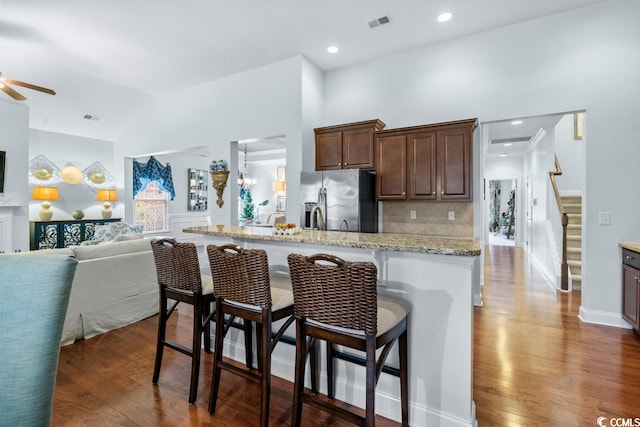 kitchen featuring dark hardwood / wood-style floors, ceiling fan with notable chandelier, a breakfast bar area, and stainless steel fridge