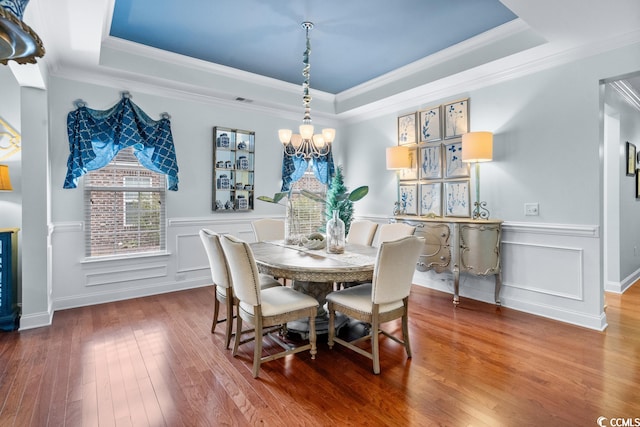 dining room featuring an inviting chandelier, ornamental molding, a raised ceiling, and dark wood-type flooring