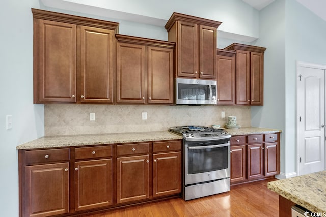 kitchen with light wood-type flooring, light stone counters, gas range, and tasteful backsplash