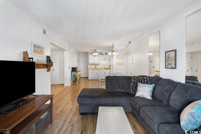 living room with ornamental molding, light hardwood / wood-style floors, and ceiling fan with notable chandelier