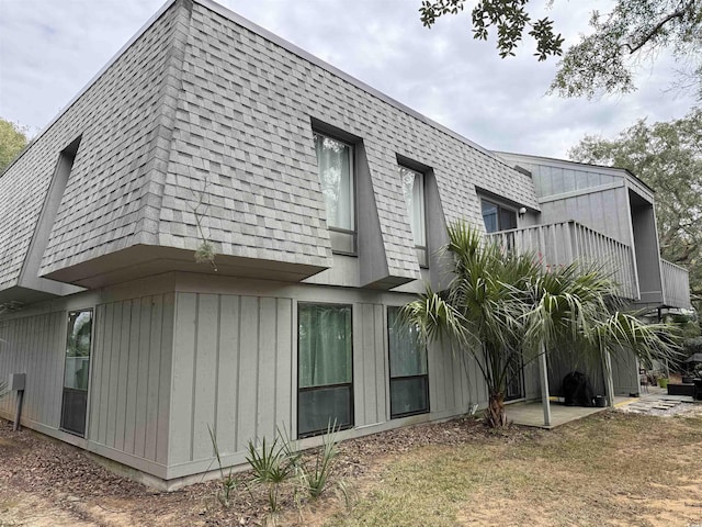 view of side of property with mansard roof, a balcony, and a shingled roof