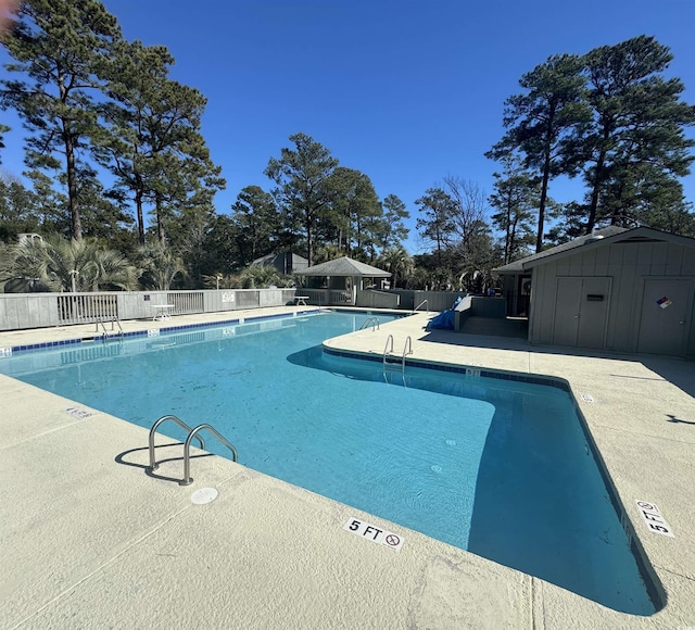 community pool featuring fence, an outdoor structure, a storage unit, and a patio