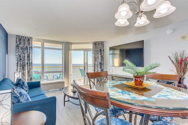 dining area featuring expansive windows, a notable chandelier, light hardwood / wood-style floors, a water view, and a textured ceiling