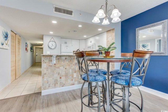 kitchen with light tile floors, decorative light fixtures, a notable chandelier, refrigerator, and white cabinets