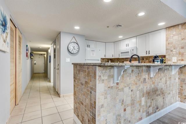 kitchen featuring white appliances, light tile floors, light stone counters, a textured ceiling, and white cabinetry