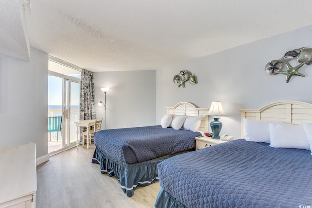 bedroom with a water view, access to outside, light hardwood / wood-style floors, and a textured ceiling