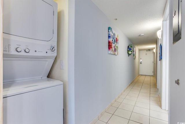 laundry room featuring a textured ceiling, stacked washer / drying machine, and light tile floors