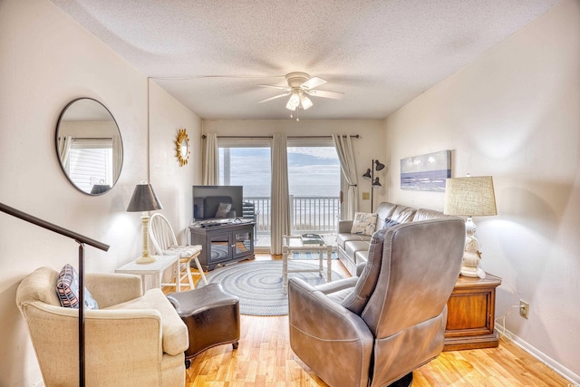 living room with light hardwood / wood-style floors, ceiling fan, and a textured ceiling