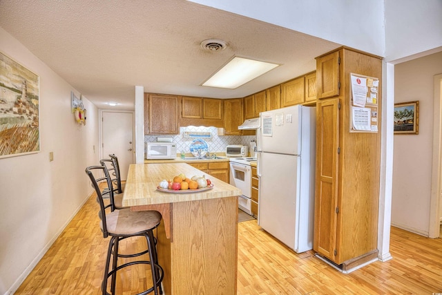 kitchen featuring white appliances, a kitchen bar, light hardwood / wood-style floors, a textured ceiling, and a kitchen island