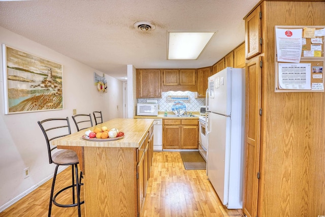 kitchen featuring white appliances, light hardwood / wood-style flooring, a kitchen island, and a kitchen breakfast bar