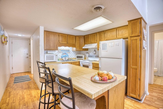 kitchen featuring white appliances, a kitchen bar, light hardwood / wood-style floors, a textured ceiling, and tasteful backsplash